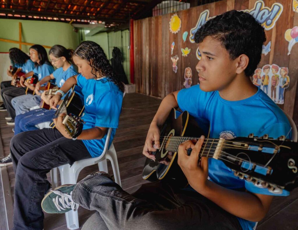 Five students at CBC sitting in a row each with a guitar, playing.